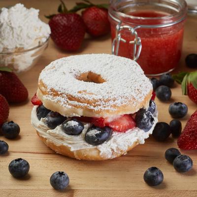 Strawberry and blueberry parfait donut surrounded by scattered berries, jam, and whipped cream.