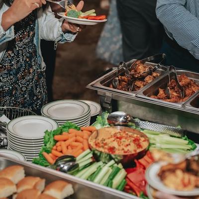 Buffet table with vegetables, dip, bread rolls, and trays of hot food.