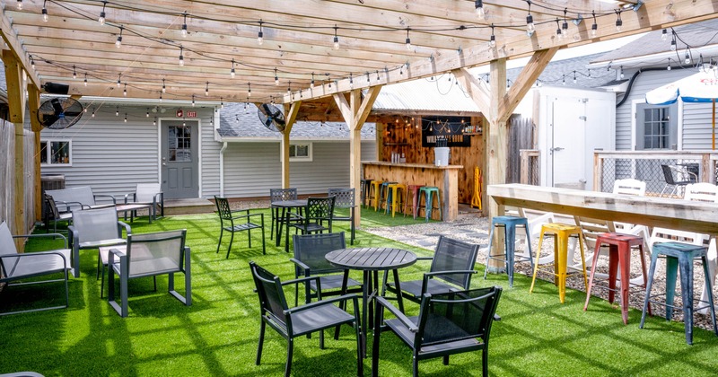 Outdoor seating area with a wooden pergola, string lights, black chairs, and a colorful bar
