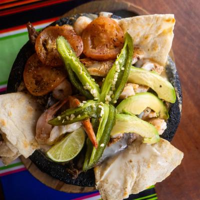Molcajete dish featuring a blend of grilled meats, vegetables and seafood.