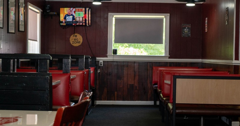 Interior, seating booths with tables on the left and right, carpet flooring, TV on the wall