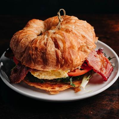 Croissant breakfast sandwich with bacon, egg, and tomato.