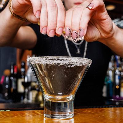 Bartender squeezing citrus over a cocktail glass with a salted rim.