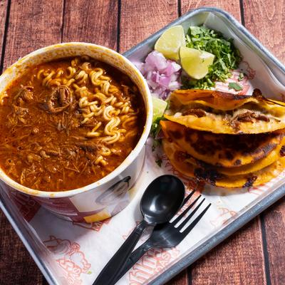 Birria ramen noodles served with two quesabirria tacos, chopped cilantro, onions, and limes.