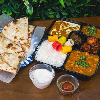 Indian thali meal with naan, basmati rice, butter curry, chickpea curry, raita, and gulab jamun.