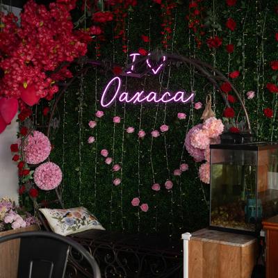 Dense green hedge wall adorned with red and pink roses and a neon sign.