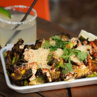 Elote-style Brussels sprouts served on the table alongside a Margarita cocktail.