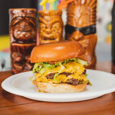 Mana Burger plate served on a table with tiki mugs in the background.