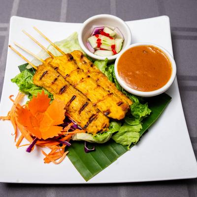Grilled papaya skewers on a square plate, with peanut sauce and cucumber salad in bowls.