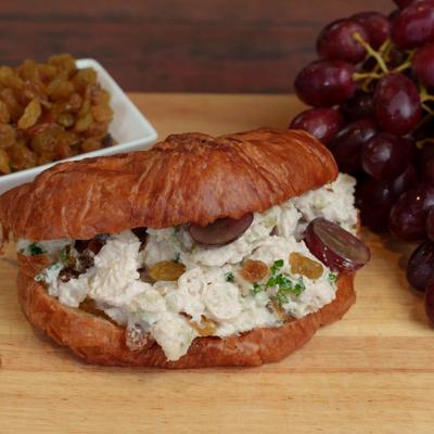 Pulled chicken salad sandwich accompanied with raisins and fresh grapes on the table.