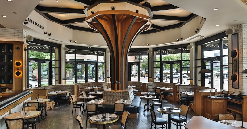 A modern interior - a central wooden column, black chairs, wood tables and large windows