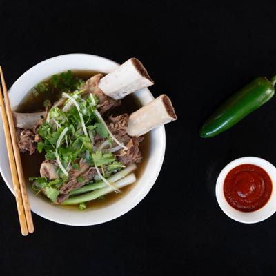 Short rib pho with herbs and broth in bowl, accompanied by dipping sauce.
