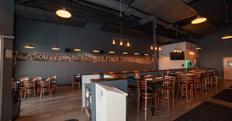 Interior of a taphouse with wooden furniture, pendant lighting, and a large mural on the back wall.