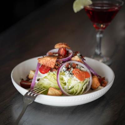 Wedge salad with blue cheese dressing served alongside a cocktail in a martini glass.