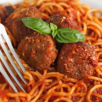 Spaghetti with meatballs in marinara sauce, garnished with fresh basil, close-up.