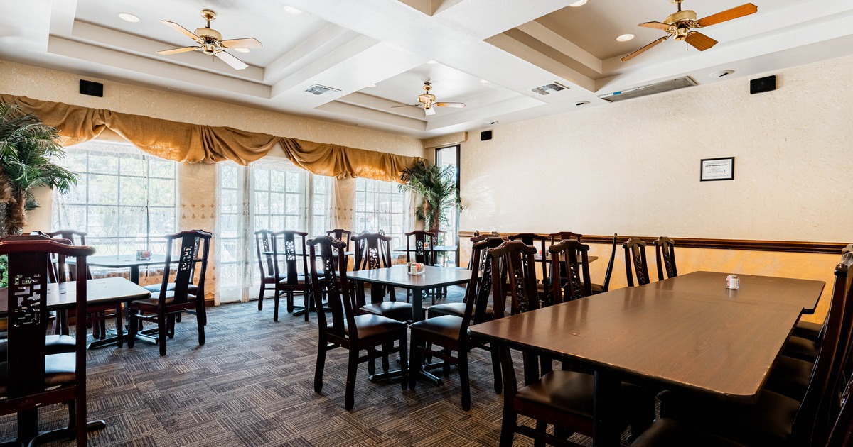 A cozy restaurant interior featuring wooden tables and chairs, ceiling fans, and large windows