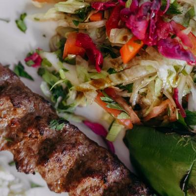 Grilled lamb kebab with fresh salad and a roasted green pepper on a plate.