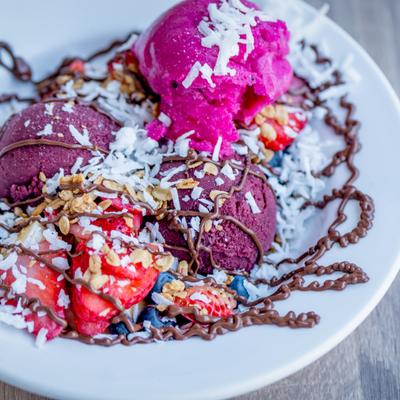 Acai bowl  topped with shredded coconut, granola, sliced strawberries, and chocolate drizzle.