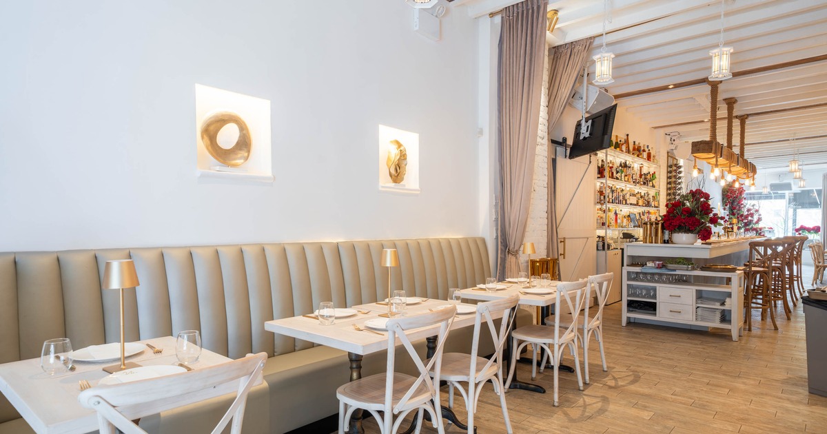 Modern restaurant interior with gray booths and a bar counter, featuring artistic wall decor and elegant table settings