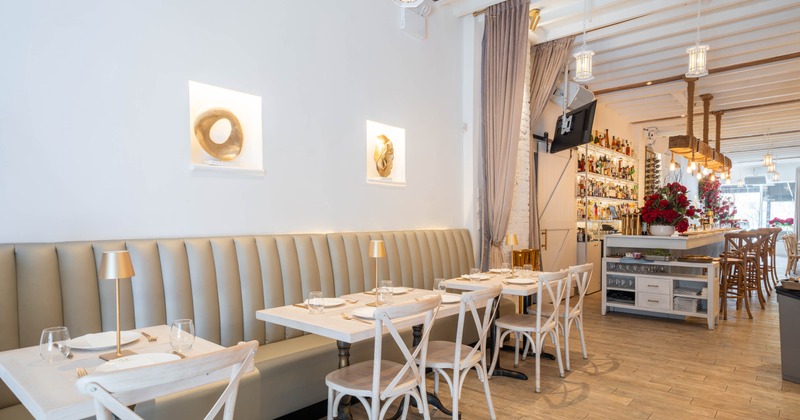 Modern restaurant interior with gray booths and a bar counter, featuring artistic wall decor and elegant table settings