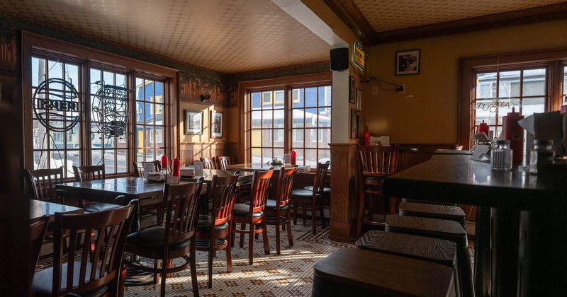 Interior, dining and bar area, tables with chairs, bar with stools on the right, tile flooring