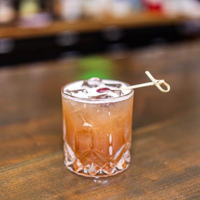 Brown cocktail on the rocks, garnished with a cherry.