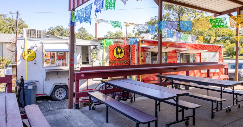 Outdoor area with picnic tables and colorful banners, featuring two food trucks in the background