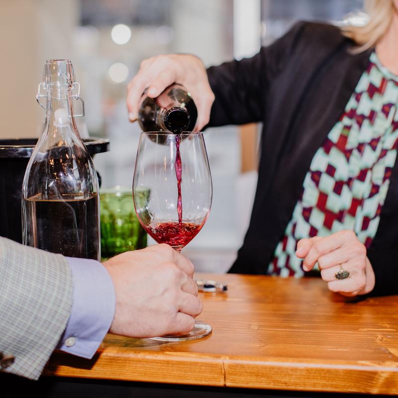 Person pouring red wine into glass on the counter.