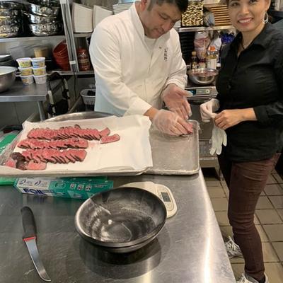 Kitchen interior, two employees plating beef on a tray.
