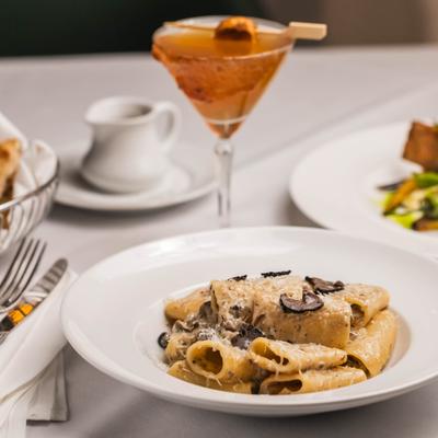 Pasta with wild mushrooms, black truffles, and grated cheese served with a cocktail.