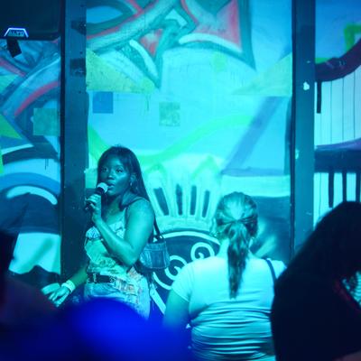 Performer singing on stage with colorful mural background.