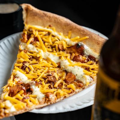 A slice of pizza with chicken, bacon, mozzarella, cheddar, and ranch.