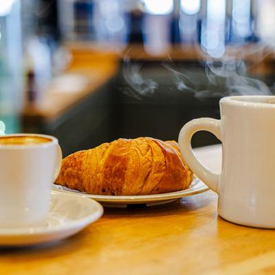 A croissant and two coffees on a wooden counter.