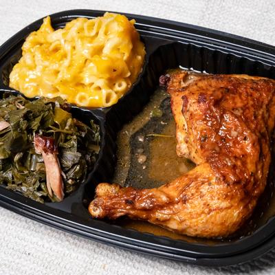 Takeout container with baked chicken, macaroni and cheese, and collard greens.