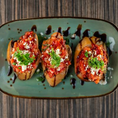 Three bruschetta topped with diced tomatoes, goat cheese, and balsamic reduction.