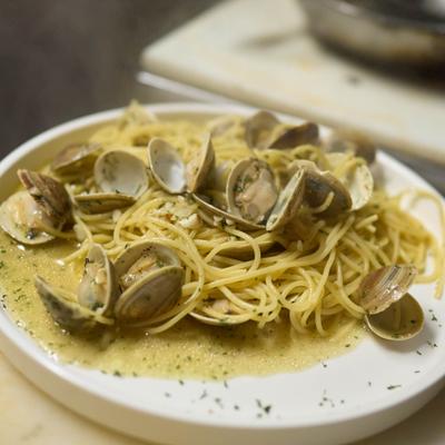 Spaghetti with clams in herb sauce on a round white plate.