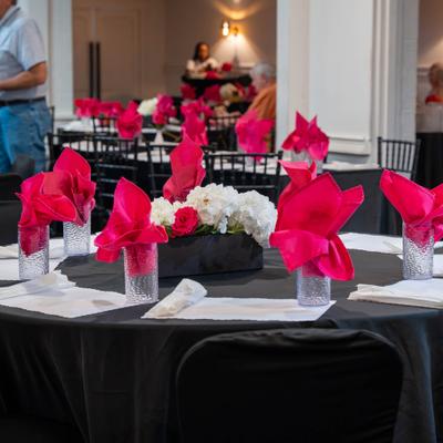 Black tables feature vibrant pink napkins and elegant white floral centerpieces indoors.