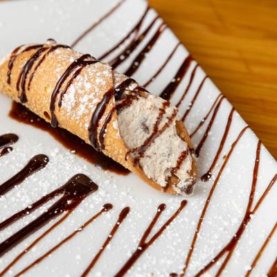 A homemade cannoli served on a plate with chocolate drizzle.