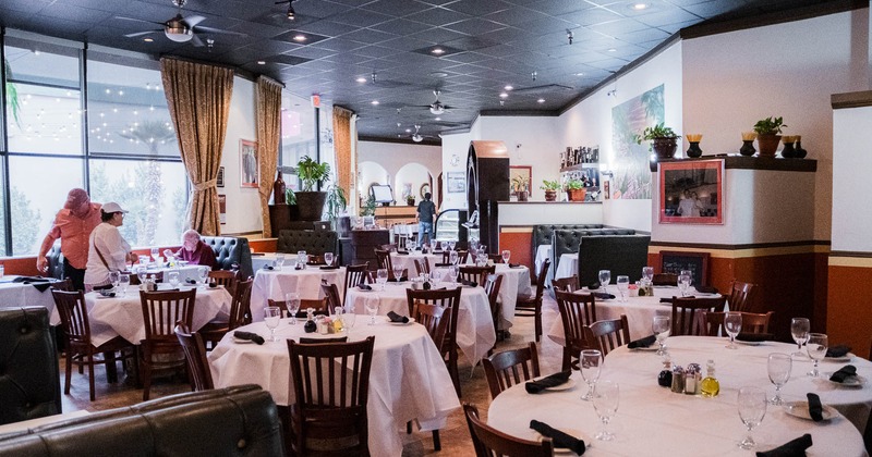 Interior of a restaurant with round tables, white tablecloths, and wooden chairs