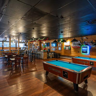 Rustic bar interior with pool tables, wooden walls, and high-top seating.