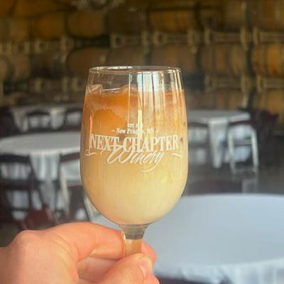 Hand holding a glass of iced coffee drink with the Next Chapter Winery logo.