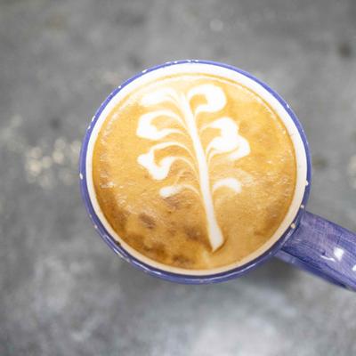 Latte with leaf art in a purple mug on stone surface.