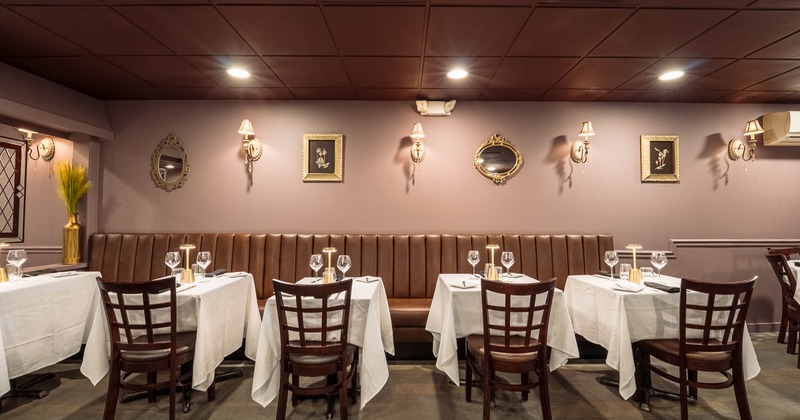 An elegant interior with brown leather seating, white tablecloths and decorative wall lights.
