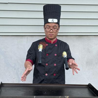 Chef performing with fire sticks in front of a grill.