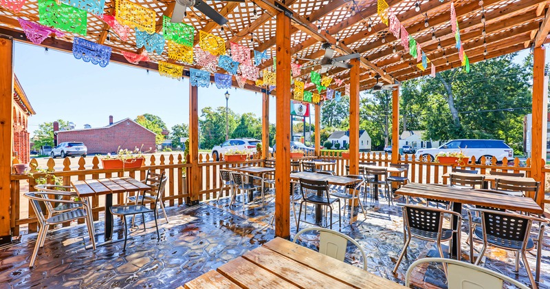 Outdoor restaurant patio with wooden tables, metal chairs, ceiling fans
