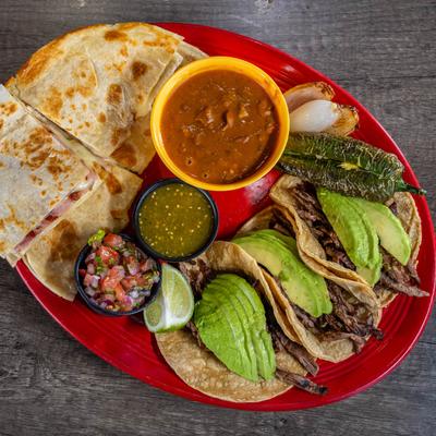 Mexican food platter with tacos, quesadillas, salsa, and avocado.