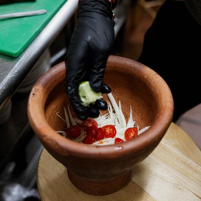 A hand adding ingredients to a clay bowl with cherry tomatoes.