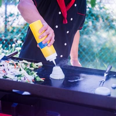 Chef squeezing sauce onto a griddle with vegetables on the side.