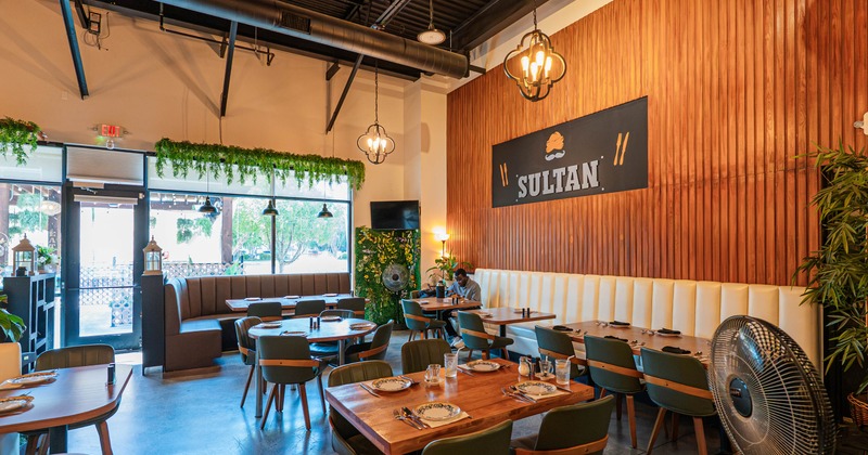 Interior of a warmly lit restaurant with wood-paneled walls, dining tables, booths, plants, sign.