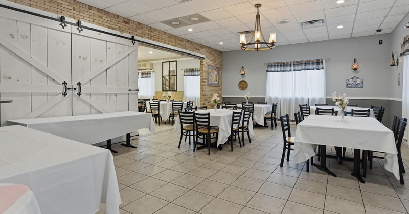 A cozy restaurant with white tablecloth covered tables and black chairs